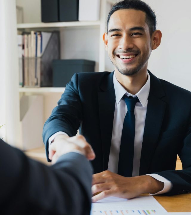 pexels-photo-12885861-12885861 Confident businessman in suit shaking hands at office desk, symbolizing successful partnership.